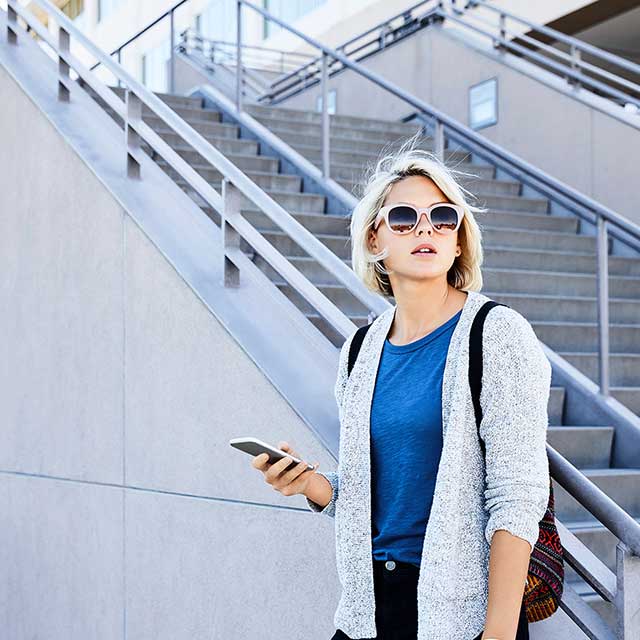 Woman holding a phone and waiting near a stair case.