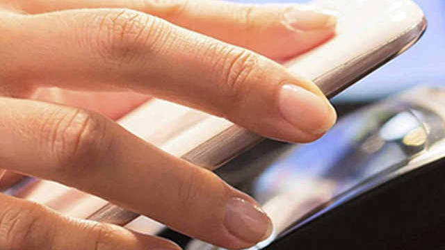 Close up of a hand holding a mobile phone next to a payment terminal.